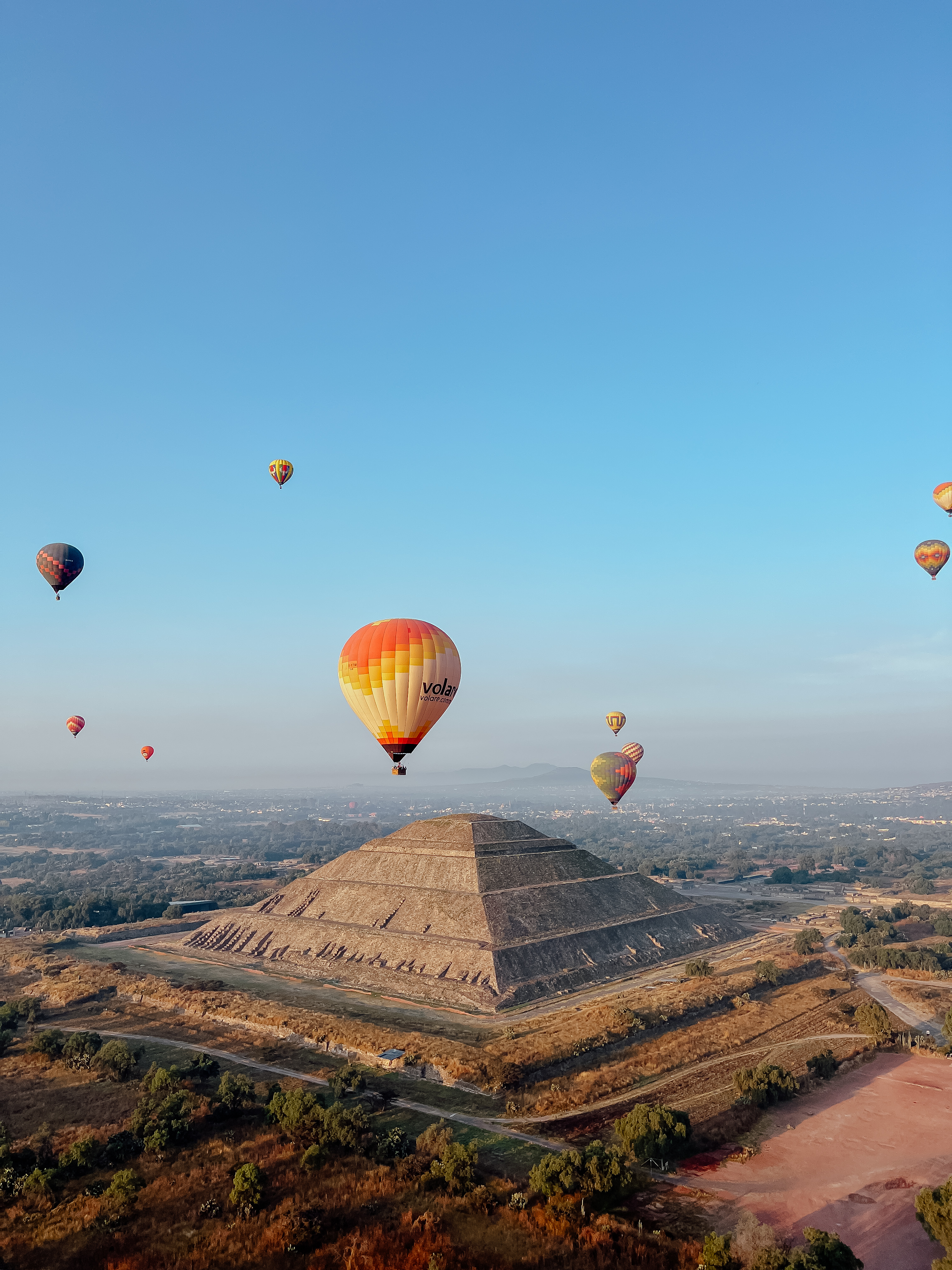 Hot air balloons floating above an ancient pyramid at sunrise