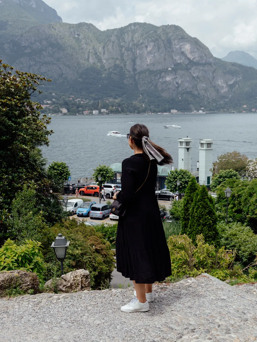 A traveller looking out across Lake Como to the mountains beyond, from a garden terrace above the waterfront