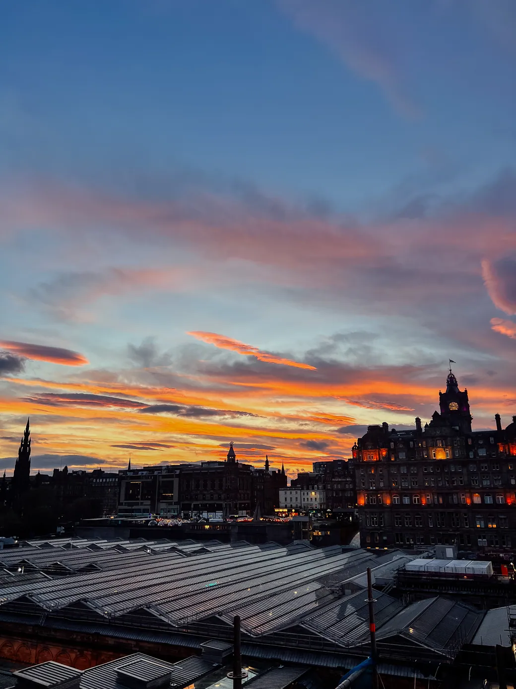 Edinburgh rooftops and the Balmoral clock tower beneath a vivid sunset sky