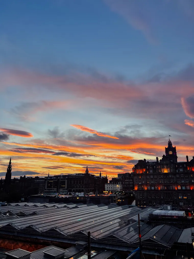 Edinburgh rooftops and the Balmoral clock tower beneath a vivid sunset sky